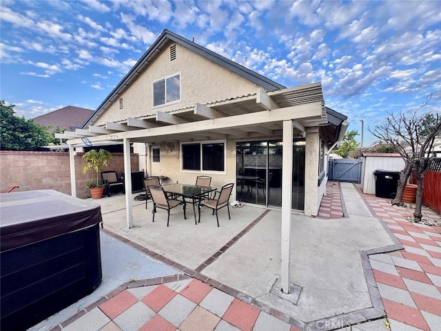 rear view of property featuring a hot tub, a fenced backyard, a patio area, a pergola, and stucco siding