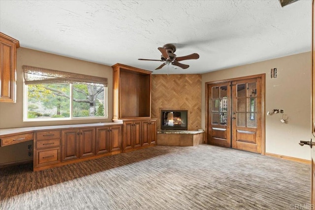 unfurnished living room with a glass covered fireplace, light colored carpet, built in desk, and a textured ceiling