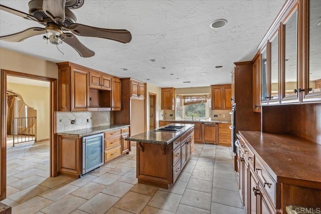 kitchen with beverage cooler, stainless steel gas cooktop, a kitchen island, backsplash, and brown cabinets