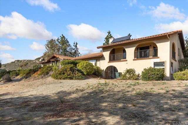 back of property featuring a tiled roof, a chimney, a balcony, and stucco siding