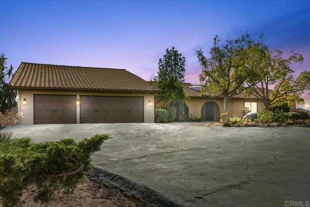 view of front of property featuring a garage, a tiled roof, driveway, and stucco siding