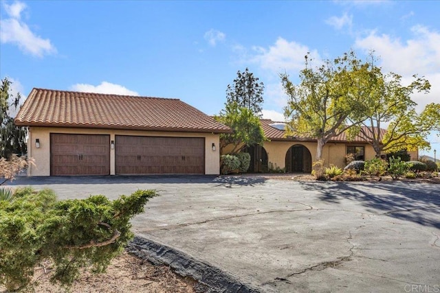 mediterranean / spanish-style house with a garage, a tile roof, and stucco siding