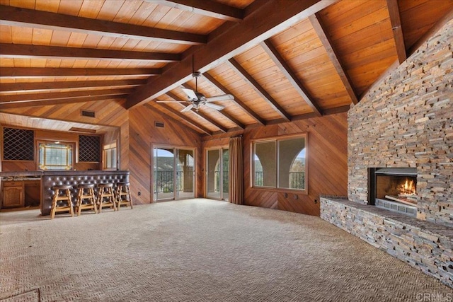 unfurnished living room featuring a dry bar, vaulted ceiling with beams, a stone fireplace, carpet floors, and wood walls