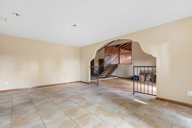 unfurnished living room featuring baseboards, stairs, and arched walkways