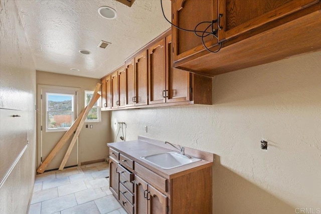 kitchen featuring visible vents, brown cabinetry, light countertops, a textured ceiling, and a sink