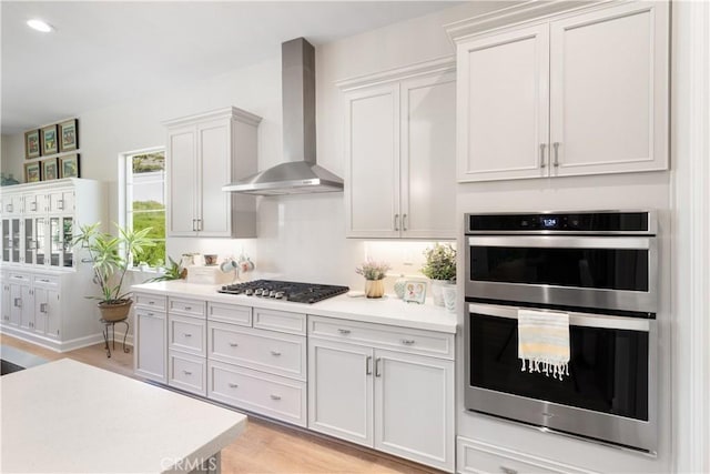 24674 Crestley Dr, Corona, CA 92883 - kitchen featuring wall chimney exhaust hood, appliances with stainless steel finishes, light countertops, light wood-style flooring, and white cabinets