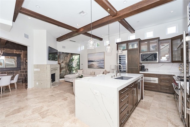 kitchen with a tiled fireplace, a sink, built in microwave, dark brown cabinets, and beam ceiling