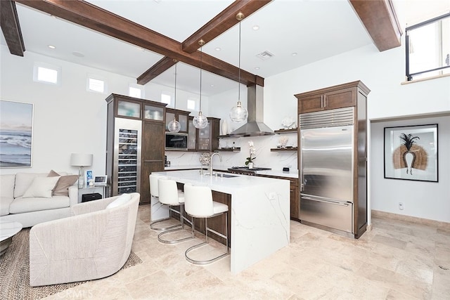 kitchen with wall chimney exhaust hood, light countertops, built in fridge, and beam ceiling