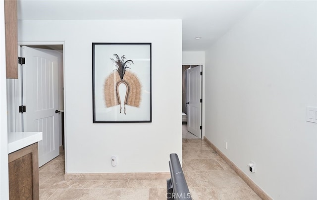 hallway featuring stone finish flooring and baseboards