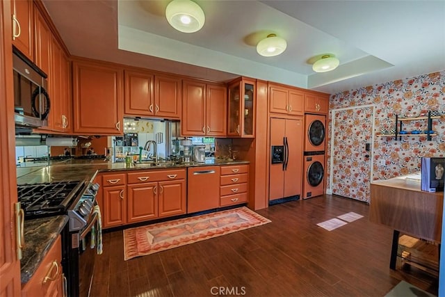 kitchen with a tray ceiling, stacked washer and dryer, brown cabinets, and appliances with stainless steel finishes