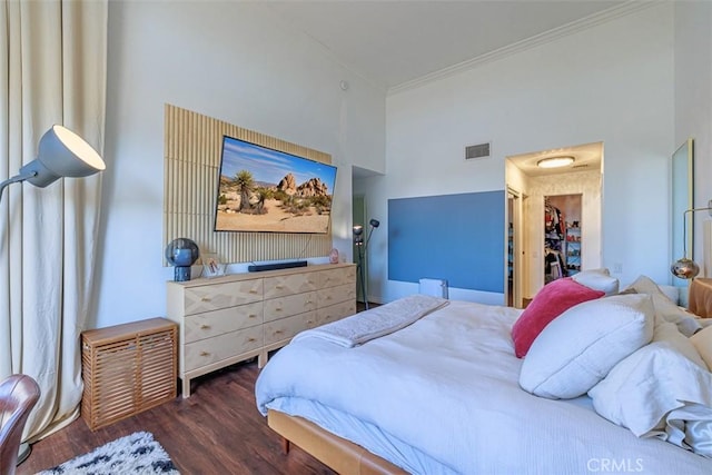 bedroom featuring visible vents, wood finished floors, a high ceiling, crown molding, and a spacious closet