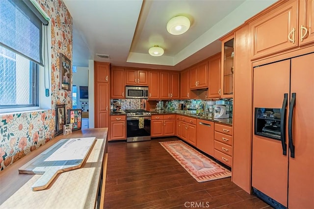 kitchen with visible vents, wallpapered walls, a tray ceiling, dark wood finished floors, and appliances with stainless steel finishes