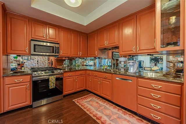 kitchen with a tray ceiling, backsplash, dark wood-style floors, dark stone counters, and appliances with stainless steel finishes