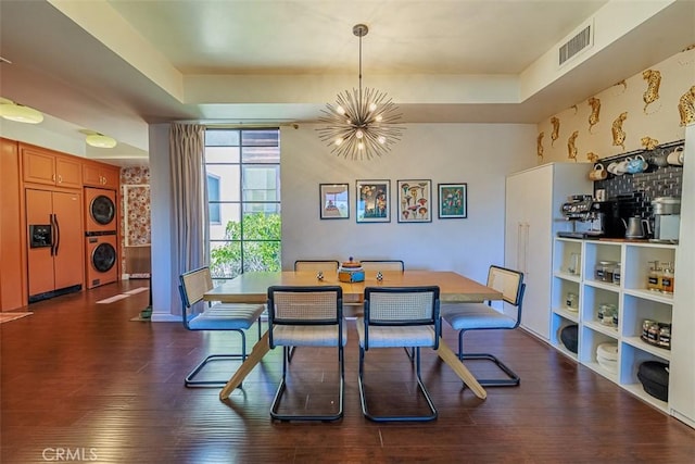 dining space featuring visible vents, stacked washer / drying machine, an inviting chandelier, and wood finished floors