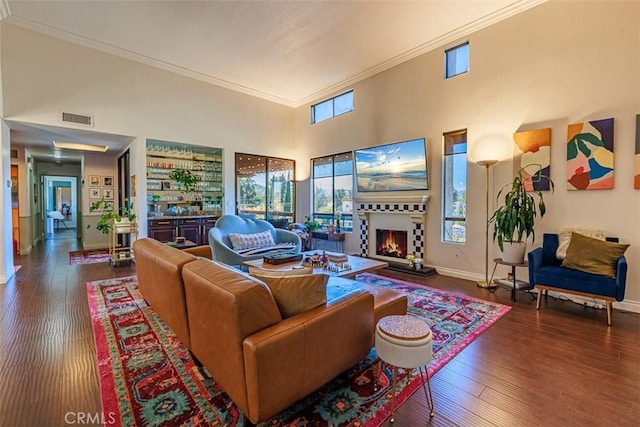 living area featuring visible vents, ornamental molding, hardwood / wood-style flooring, a warm lit fireplace, and a towering ceiling