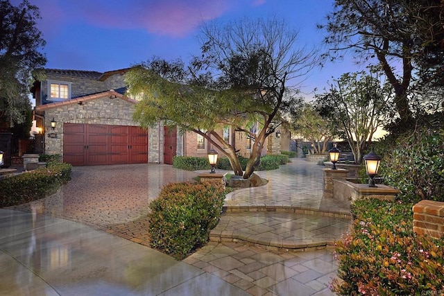 view of front of house featuring decorative driveway, stone siding, and a garage