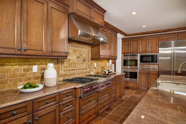 kitchen featuring under cabinet range hood, built in appliances, brown cabinetry, and dark tile patterned flooring