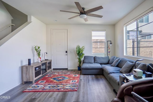 living area with a ceiling fan, stairway, baseboards, and wood finished floors