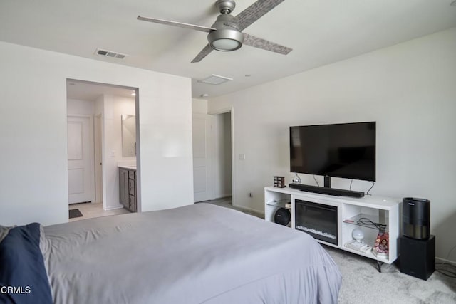 bedroom with light colored carpet, visible vents, attic access, ceiling fan, and ensuite bath