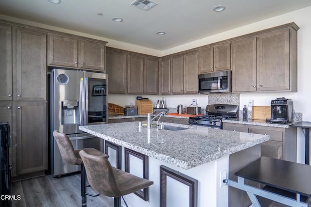kitchen featuring visible vents, dark wood-style floors, appliances with stainless steel finishes, a breakfast bar, and a sink