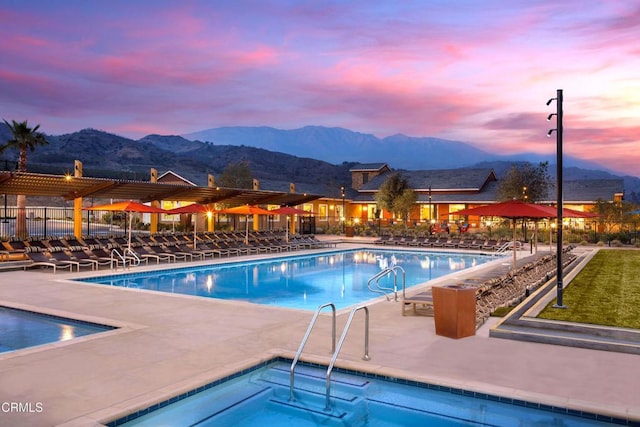 pool at dusk featuring a patio area, fence, a community pool, and a mountain view