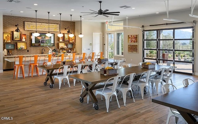 dining space with visible vents, a ceiling fan, brick wall, wood finished floors, and a high ceiling