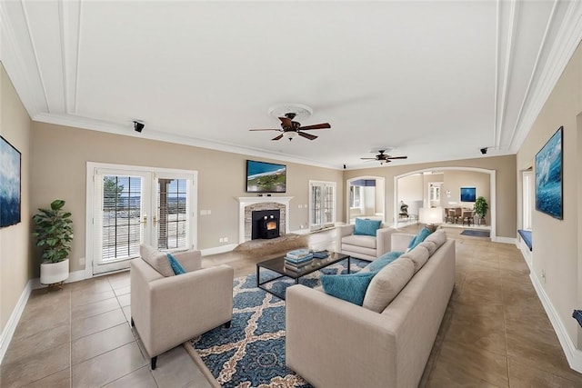 living room featuring baseboards, arched walkways, a fireplace with raised hearth, ornamental molding, and light tile patterned flooring