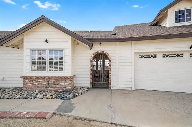 entrance to property with a garage, concrete driveway, brick siding, and a shingled roof