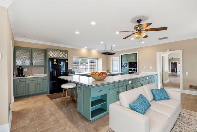 kitchen featuring light tile patterned floors, green cabinets, light countertops, black fridge, and an island with sink