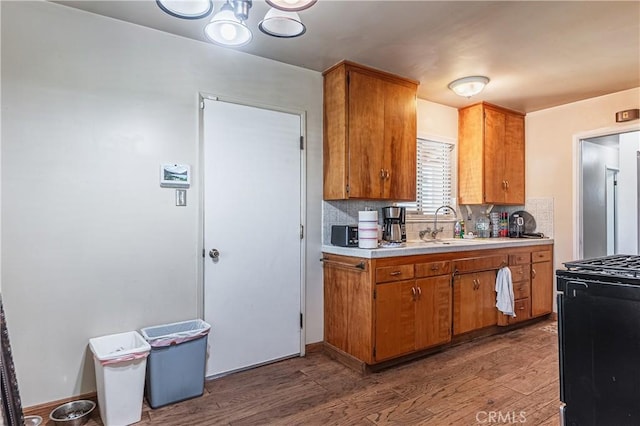 kitchen with light countertops, black gas range oven, decorative backsplash, brown cabinetry, and wood finished floors