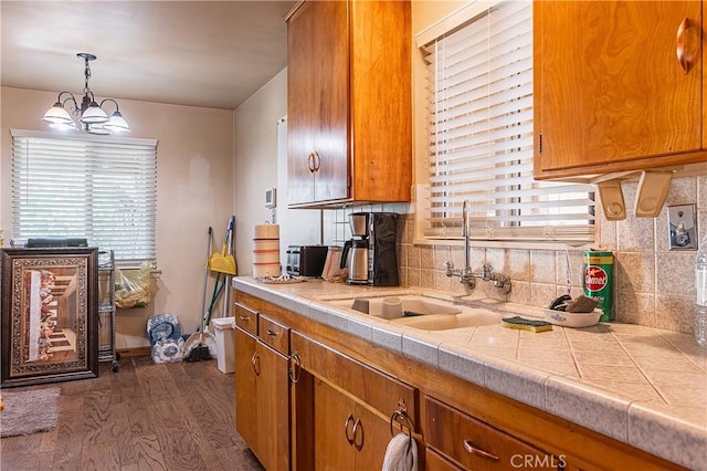 kitchen with brown cabinetry, dark wood finished floors, a sink, and backsplash