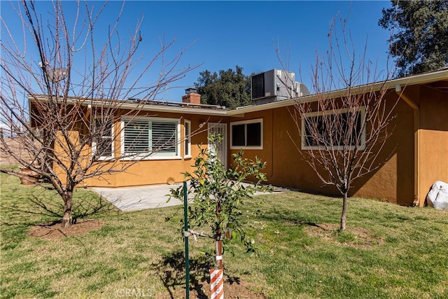 exterior space featuring central AC unit, a chimney, a front yard, and stucco siding