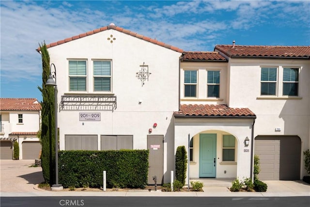 mediterranean / spanish-style home with a tile roof, a garage, stucco siding, and concrete driveway