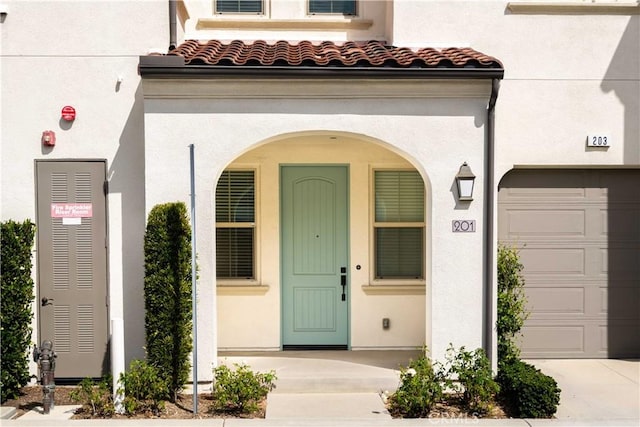view of exterior entry with a garage, stucco siding, driveway, and a tiled roof
