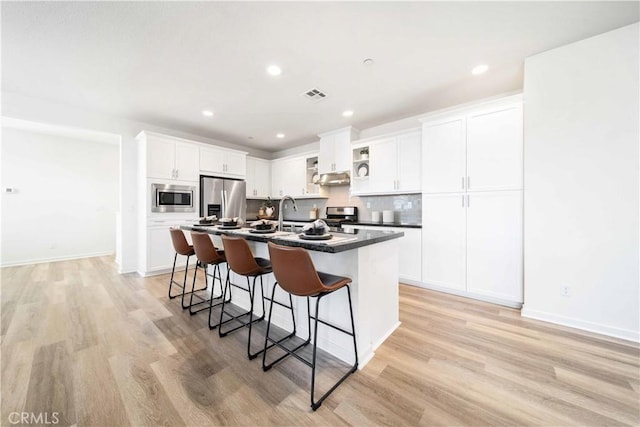 kitchen with stainless steel appliances, a breakfast bar, light wood-style floors, an island with sink, and recessed lighting