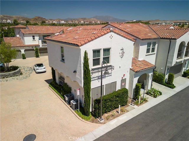 view of front of home featuring a tile roof, stucco siding, central air condition unit, driveway, and a garage