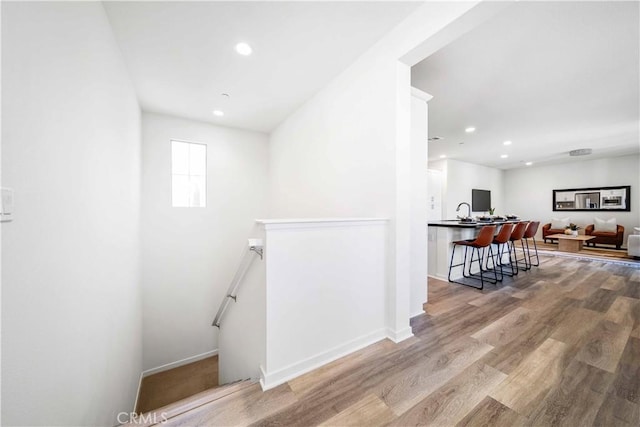 hallway featuring an upstairs landing, wood finished floors, recessed lighting, and baseboards