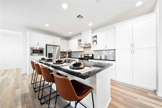 kitchen featuring appliances with stainless steel finishes, dark countertops, a kitchen breakfast bar, a kitchen island with sink, and white cabinets