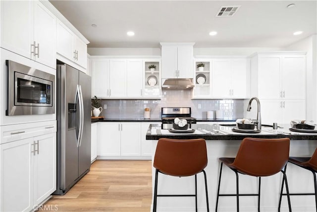 kitchen featuring appliances with stainless steel finishes, a kitchen breakfast bar, under cabinet range hood, a sink, and white cabinetry