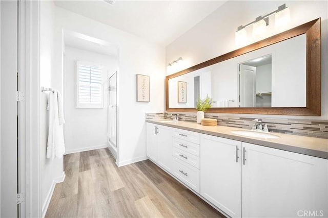 full bath with decorative backsplash, wood finished floors, baseboards, double vanity, and a shower stall