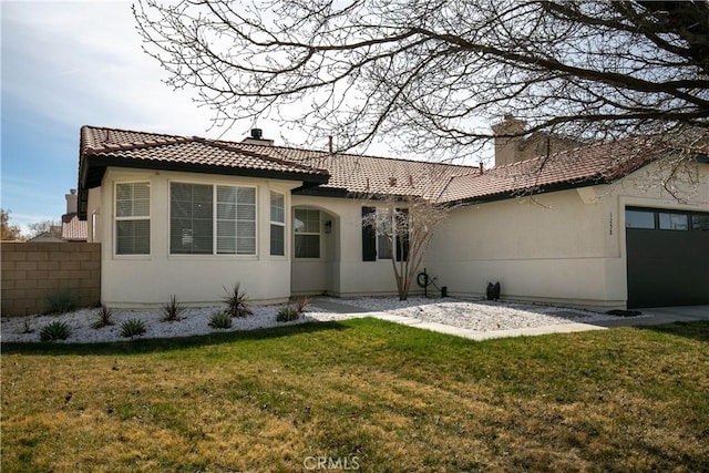 rear view of house featuring a chimney, a tiled roof, fence, a yard, and stucco siding