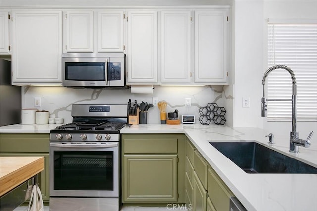 kitchen with green cabinetry, backsplash, stainless steel appliances, white cabinetry, and a sink