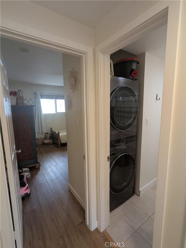 clothes washing area featuring light wood-type flooring, stacked washer and dryer, baseboards, and laundry area