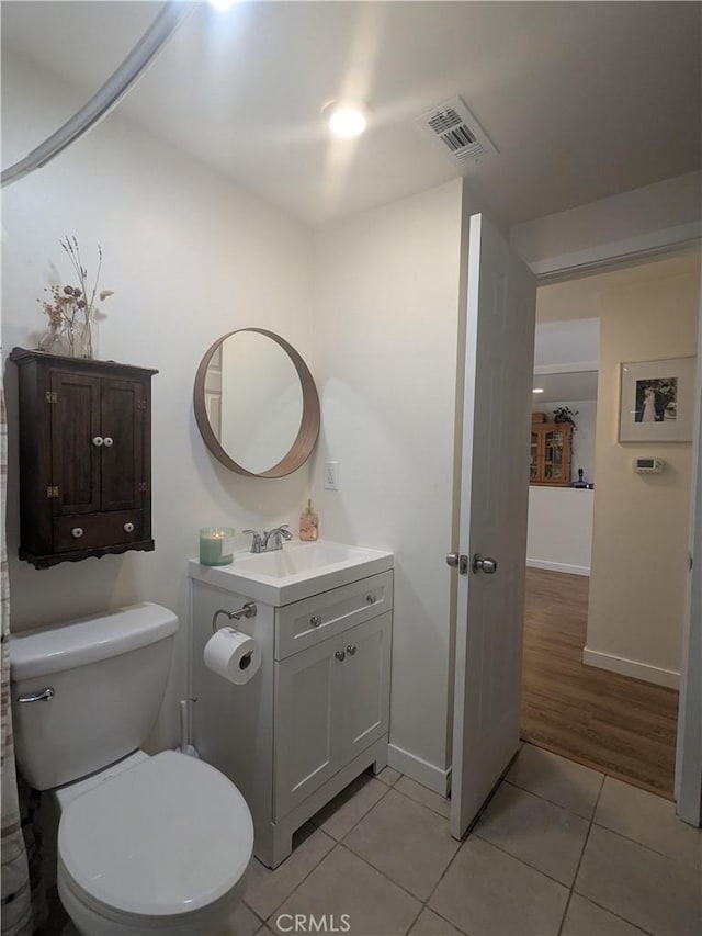 half bath with baseboards, visible vents, toilet, tile patterned floors, and vanity