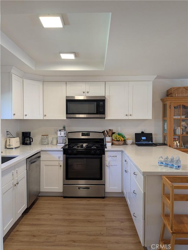 kitchen featuring white cabinets, a peninsula, stainless steel appliances, light countertops, and light wood-style floors