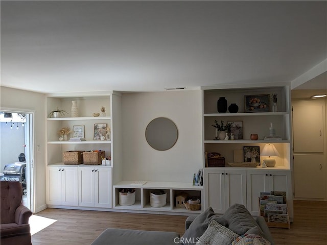 living area with built in shelves, visible vents, and wood finished floors