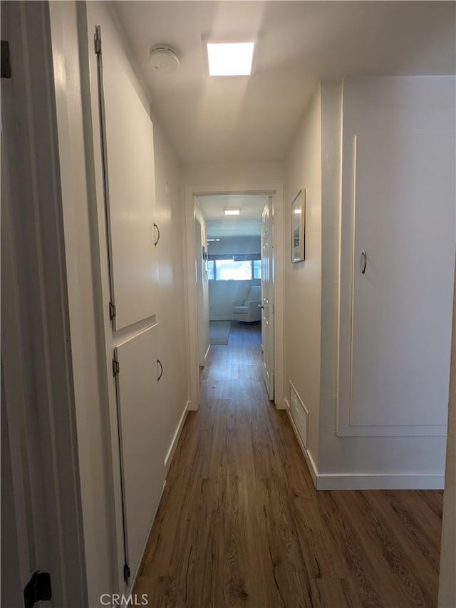 hallway featuring visible vents, baseboards, and wood finished floors