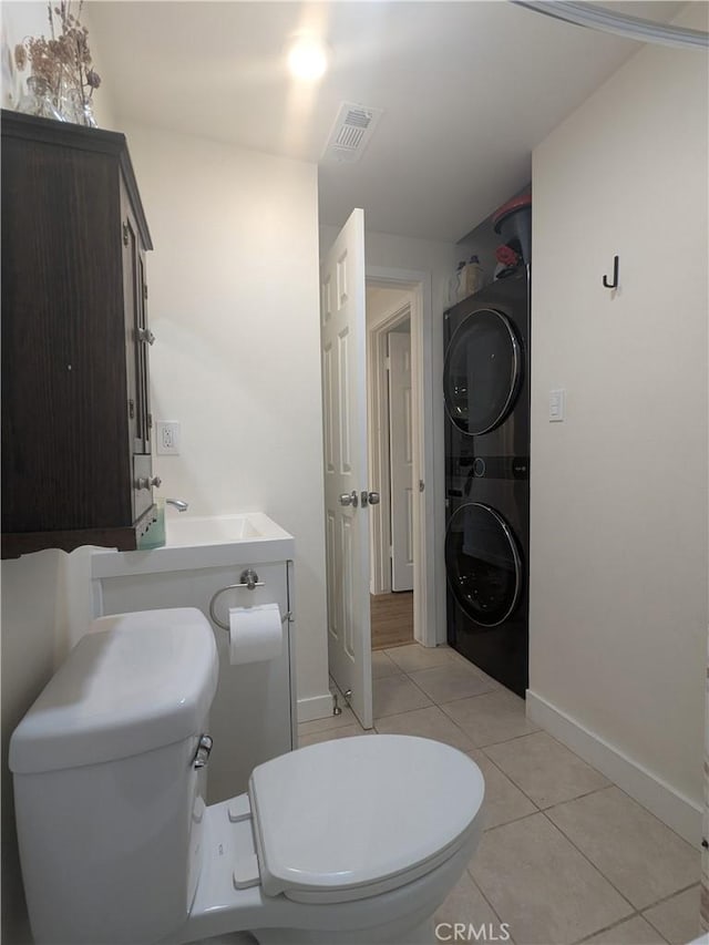 bathroom featuring stacked washer and dryer, a sink, toilet, and tile patterned floors