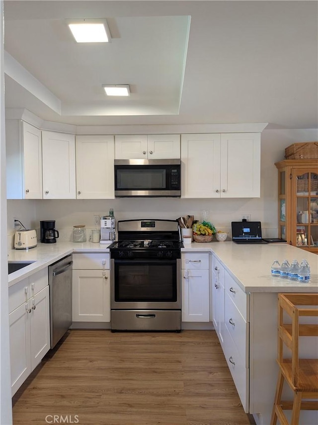 kitchen featuring stainless steel appliances, light wood-type flooring, white cabinets, and a peninsula