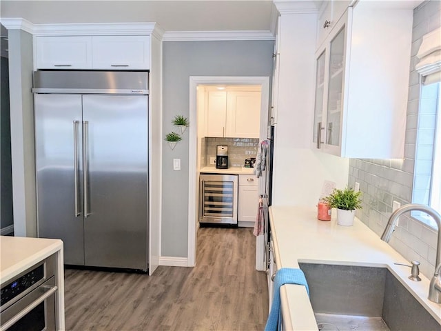 kitchen with built in fridge, ornamental molding, white cabinetry, a sink, and beverage cooler